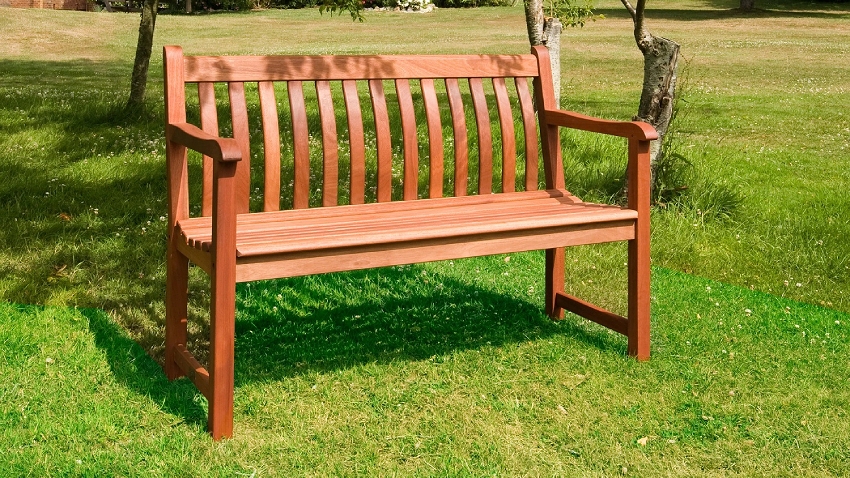 Alexander Rose Cornis Broadfield Bench 4ft 334B in oiled mahogany hardwood positioned on a lawn in a landscaped garden setting