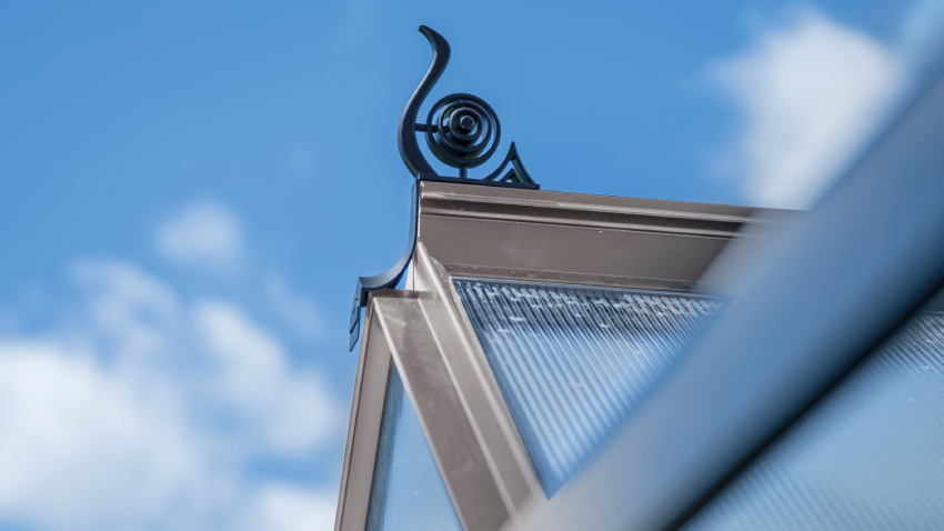 Close-up of a Halls ICON 6 6x4 Greenhouse, with black roof cresting, polycarbonate glazing and a mill aluminium frame.