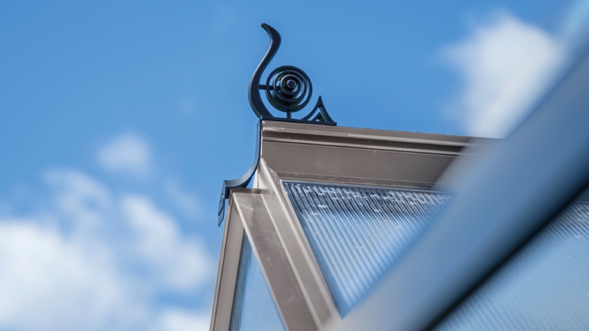 Close-up of a Halls ICON 6 6x10 Greenhouse, with black roof cresting, polycarbonate glazing and a mill aluminium frame.