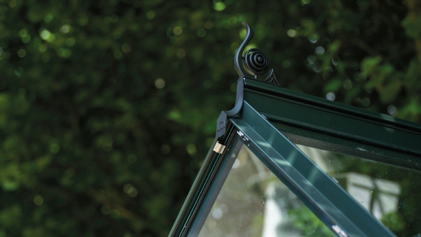 Close-up of a Halls ICON 6 6x10 Greenhouse, with black roof cresting, toughened glass and a powder-coated green aluminium frame.