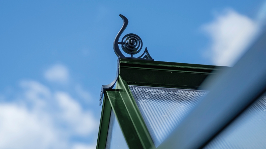 Close-up of a Halls ICON 6 6x10 Greenhouse, with black roof cresting, polycarbonate glazing and a powder-coated green aluminium frame.
