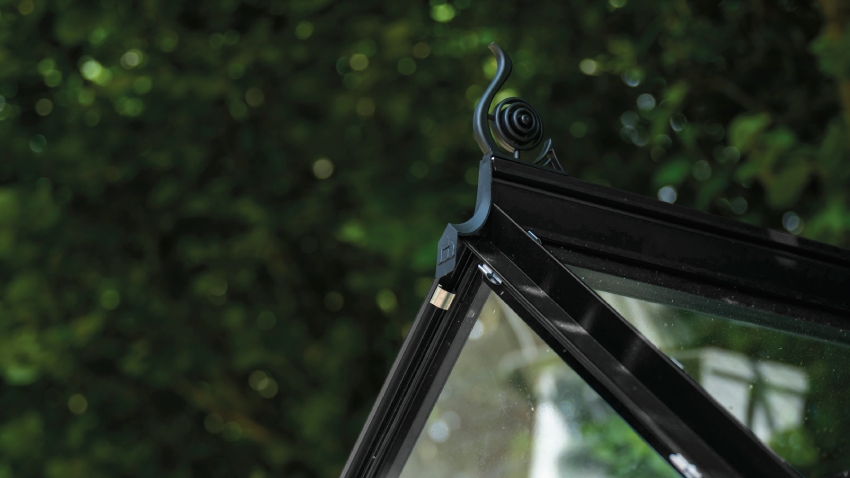 Close-up of a Halls ICON 6 6x10 Greenhouse, with black roof cresting, horticultural glass and a powder-coated black aluminium frame.