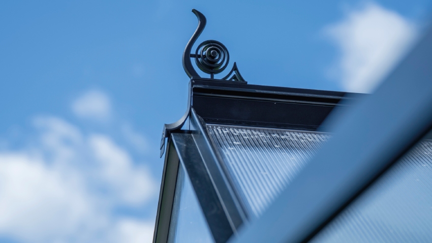 Close-up of a Halls ICON 6 6x10 Greenhouse, with black roof cresting, polycarbonate glazing and a powder-coated black aluminium frame.