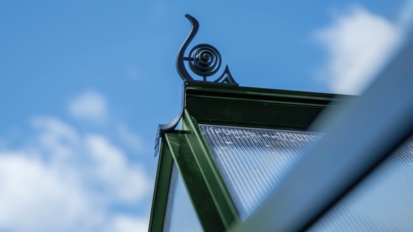 Close-up of a Halls ICON 6 6x6 Greenhouse, with black roof cresting, polycarbonate glazing and a powder-coated green aluminium frame.