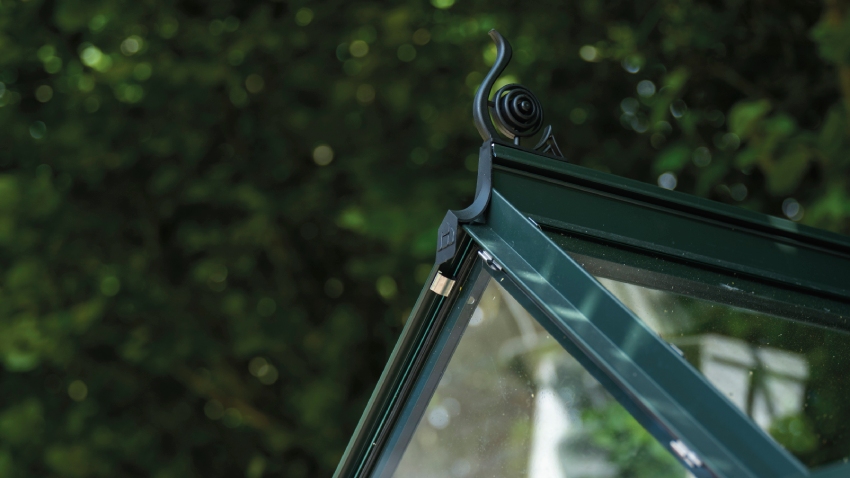 Close-up of a Halls ICON 6 6x8 Greenhouse, with black roof cresting, toughened glass and a powder-coated green aluminium frame.