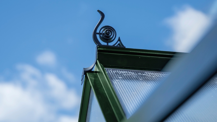 Close-up of a Halls ICON 6 6x8 Greenhouse, with black roof cresting, polycarbonate glazing and a powder-coated green aluminium frame.