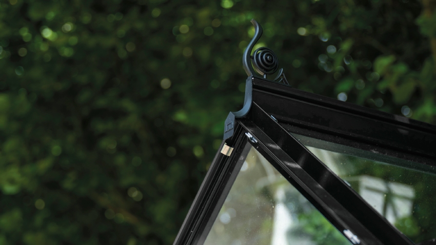 Close-up of a Halls ICON 6 6x8 Greenhouse, with black roof cresting, toughened glass and a powder-coated black aluminium frame.