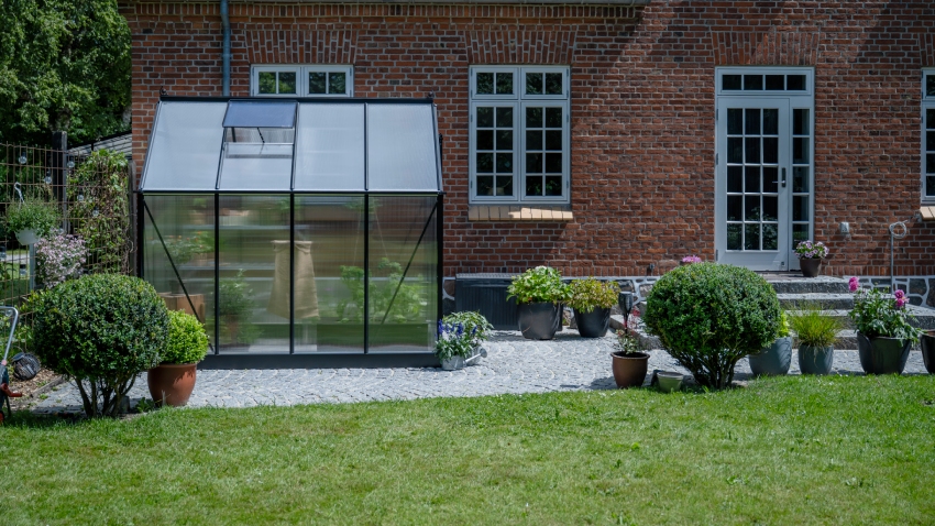 Halls ICON 6 6x8 greenhouse with black powder-coated aluminium frame and 4mm twin-wall polycarbonate glazing installed beside brick house patio