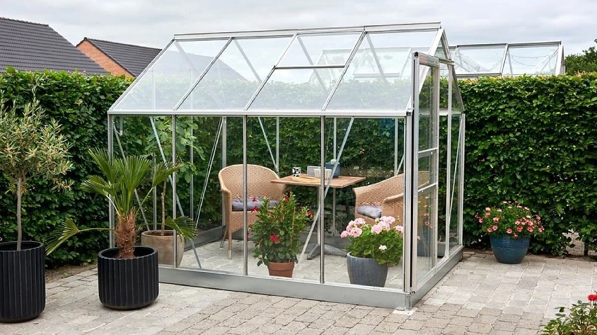 Wide-angle view of the Halls Popular 8x6 aluminium greenhouse with toughened glass, roof vent and sliding door in a landscaped garden.