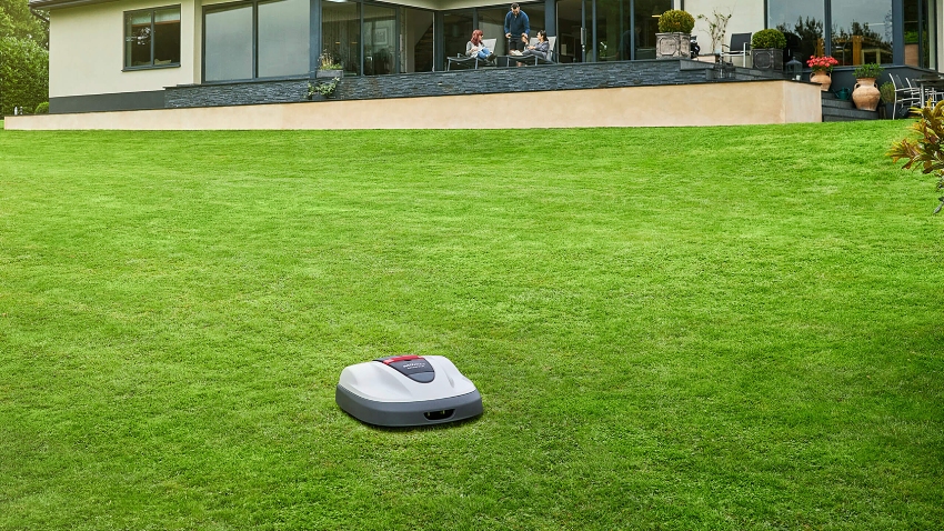 Honda Miimo HRM 310 robotic mower cutting a large residential lawn outside a modern home
