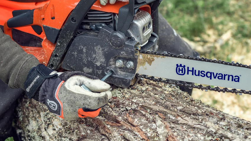 Husqvarna 135 Mark II chainsaw cutting through a log, close-up of chain and bar in action, operator wearing protective gloves, ideal for firewood cutting and garden use
