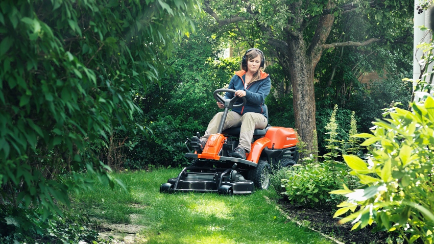 Husqvarna Rider R112C ride-on mower cutting grass around trees and garden borders with front-mounted cutting deck