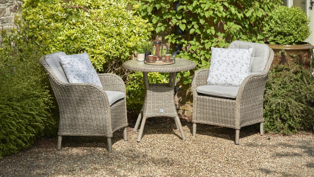Leisure Grow St Tropez Sand 2 seat garden dining set arranged outdoors, featuring two cushioned wicker armchairs and a round dining table in a garden setting.