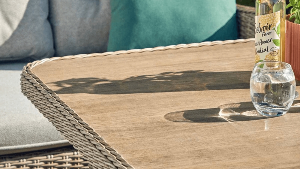 close-up of the ceramic-coated, wood-effect table top from the lg st tropez sand compact modular dining set, showing woven rattan edging and textured surface