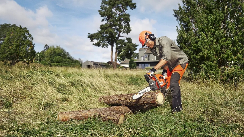Man wearing chainsaw protective helmet, gloves and trousers cutting logs with Husqvarna 435 Mark II petrol chainsaw with 15 inch bar in outdoor garden setting