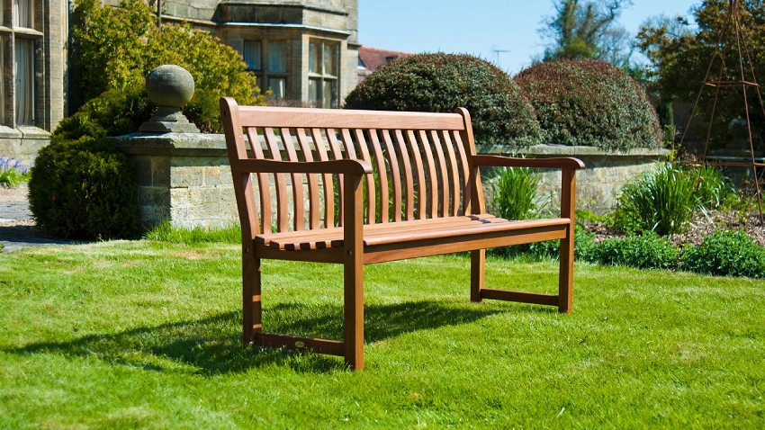 Wide view of Alexander Rose Cornis Broadfield 5ft hardwood garden bench with slatted backrest in a traditional garden setting