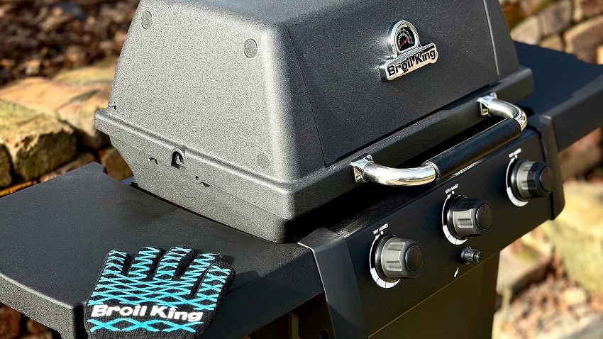 Wide-angled shot of the Broil King Gem 310 Shadow Gas BBQ, with the gas controls, grilling glove, and polished Broil King logo on display