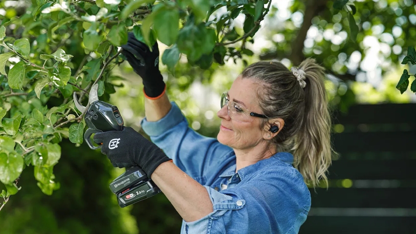 Woman using Husqvarna Aspire PS30X-P4A battery secateurs for garden pruning