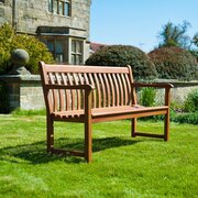 Alexander Rose Cornis Broadfield 5ft garden bench in oiled mahogany hardwood positioned on a lawn in a landscaped garden