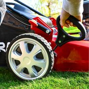 Hand adjusting cutting height lever on Cobra M46SPCVX 46cm self propelled petrol lawnmower beside rear wheel.