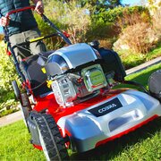Close-up of Cobra M51SPCVX 149cc petrol lawnmower engine and steel cutting deck while in use on grass.