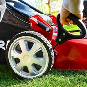 Hand adjusting cutting height lever on Cobra M51SPCVX 20 inch self propelled petrol lawnmower beside rear wheel.