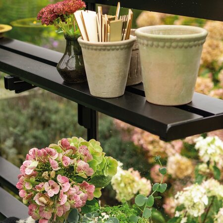 Halls modular folding shelving HR01935 inside an ICON Planthouse 8 8x12 greenhouse, holding plant pots, flowers, seed labels, and a watering can.