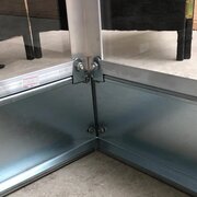 Close-up of a Halls Popular greenhouse secured to a galvanised steel base, showing corner fixings designed to improve stability and support.
