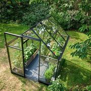 Overhead view of the Halls QUBE 68 6x8 greenhouse with black aluminium frame and toughened glass, showing internal staging, raised wooden planters, and growing crops in a compact garden setting.