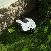 Husqvarna Automower 405XE NERA robotic lawn mower operating on grass beside a garden wall, shown in use outdoors.