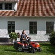Person using Husqvarna TC100i ride-on garden tractor mower cutting lawn in residential garden setting