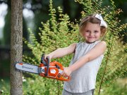 Young girl holding the Husqvarna Toy 550XP Chainsaw 546280201 beside a tree during imaginative outdoor play