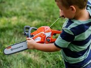 Young child using the Husqvarna Toy 550XP Chainsaw 546280201 during outdoor pretend play