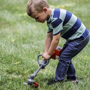 Young child using the Husqvarna Toy Grass & Weed Trimmer 546276501 during outdoor pretend garden play
