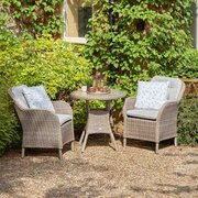 Leisure Grow St Tropez Sand 2 seat garden dining set with two cushioned rattan-effect chairs and a matching round table, styled in a leafy garden setting.