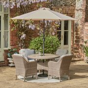 LG St Tropez Sand 4 Seat Garden Dining Set with round table, four cushioned armchairs and 2.5m parasol, shown on a summer's day.
