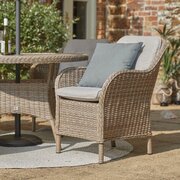 Close-up of a cushioned armchair from the LG St Tropez Sand 4 Seat Dining Set, showing woven rattan detailing and round dining table with parasol.