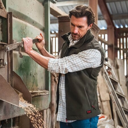 Man wearing the Hoggs of Fife Green King II men’s waterproof gilet while operating farm machinery indoors.